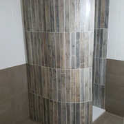 Muro curvado en ducha con azulejo imitación madera.