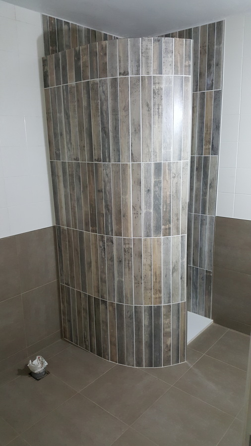 Muro curvado en ducha con azulejo imitación madera.
