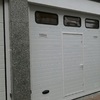 Puerta seccional en blanco con ventanas, rejillas de ventilación y puerta peatonal.